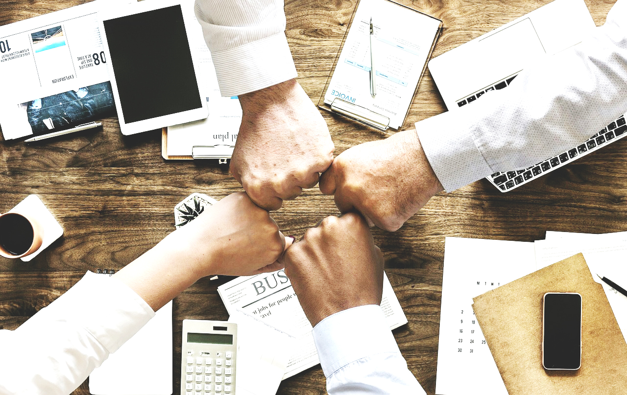 Team members fist-bumping over a desk, working together